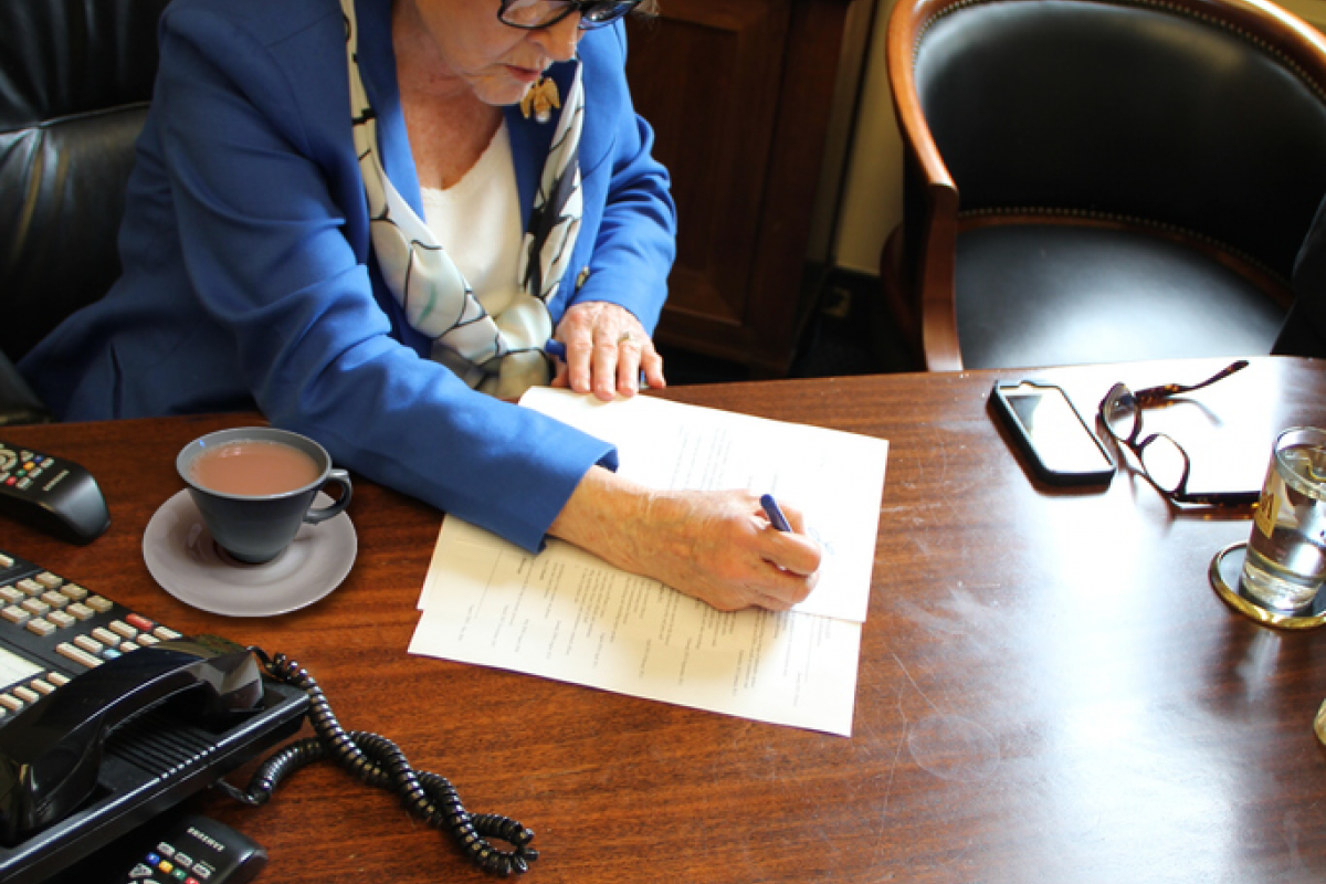 Congresswoman Louise Slaughter at a desk writing on a document with a cup of tea next to her