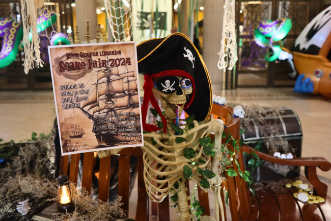 A fake skeleton dressed in a pirate hat and eye patch, holding a poster for River Campus Libraries' 2024 Scare Fair