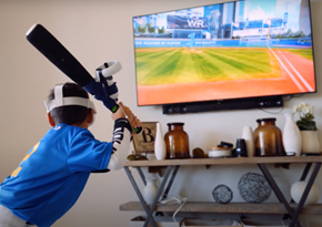 Child is at home wearing a VR headset and holding a VR baseball bat in front of a TV.