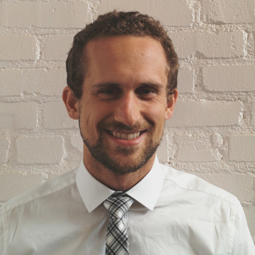 Photo of Andrew White standing against a white brick wall