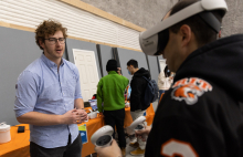 A man in a blue shirt coaches another man wearing a VR headset.