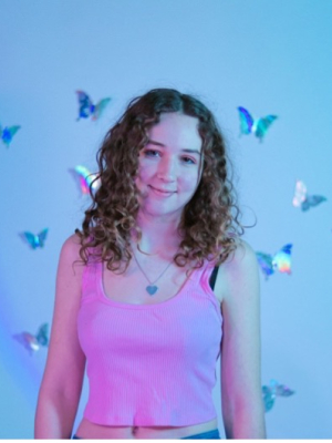 Libby Braun, person with long curly hair and tank top stands in front of a wall of butterfly decals